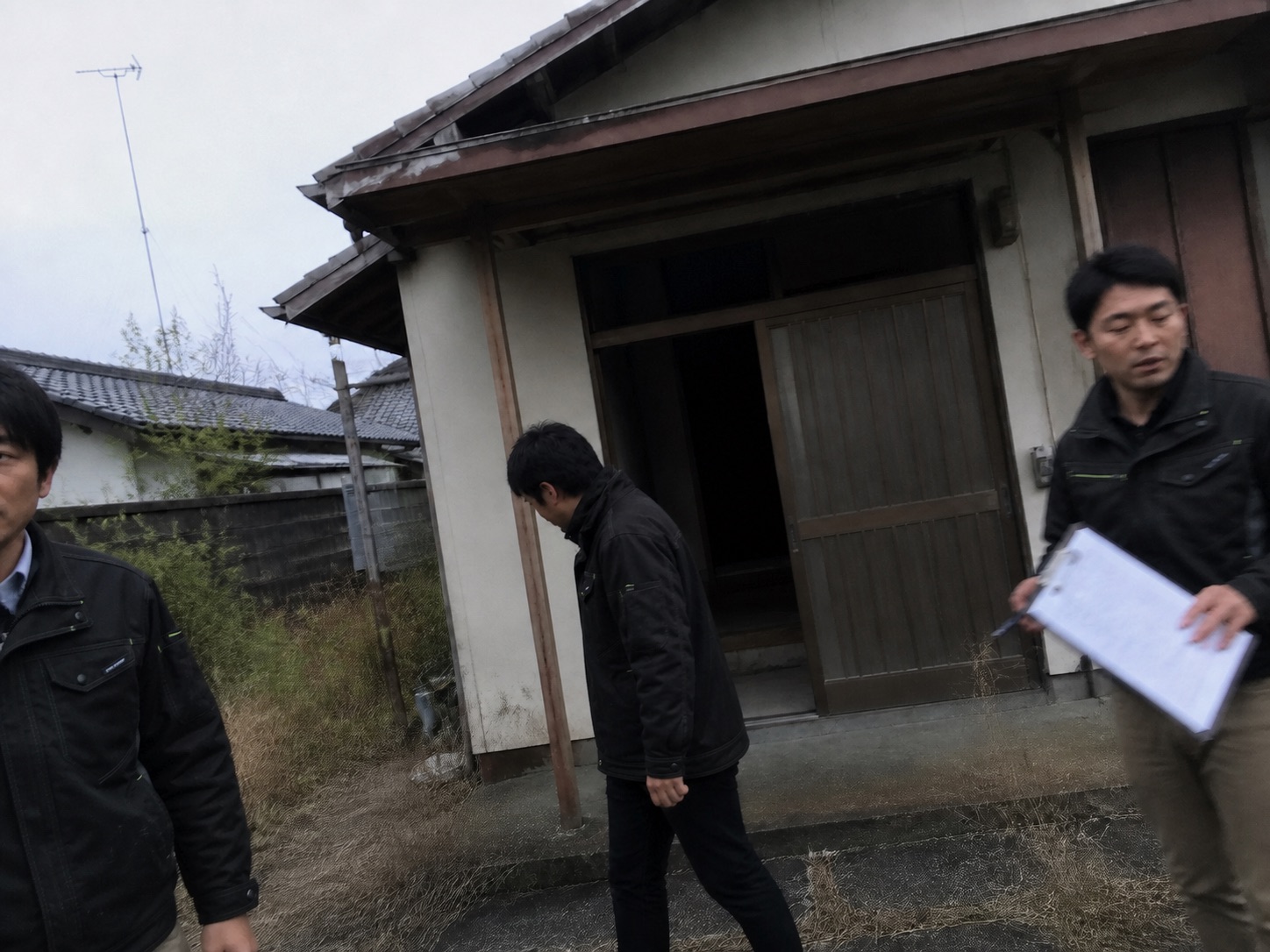 空き家の前で、担当者たちが建物を見ながら現地状況を記録する様子