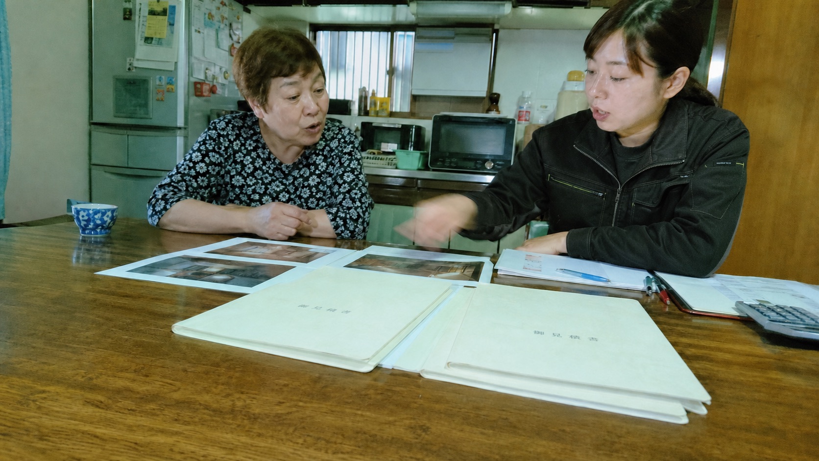 古い家の食卓で、家族と担当者が写真や見積り資料を確認する様子